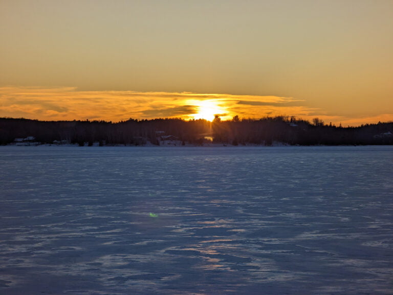A breathtaking sunset over the frozen lake, with the warm colors of the sky contrasting the cold, icy surface.